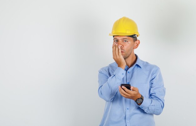 シャツの口に手で携帯電話を保持している若い男