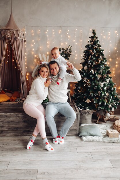 Young man holding child on his shoulders while sitting beside his beautiful wife in decorated room