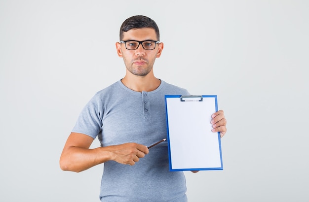 Young man holding clipboard and pencil in grey t-shirt, glasses