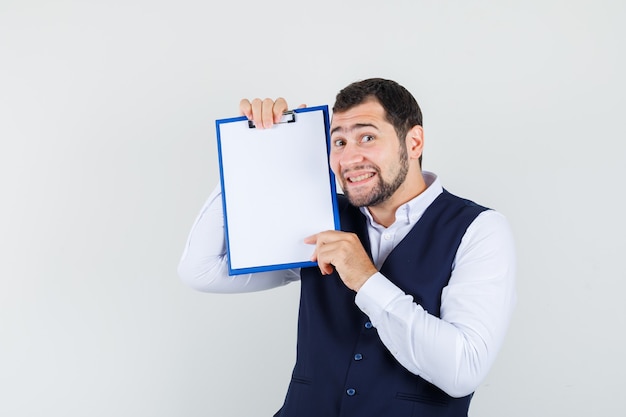 Young man holding clipboard in shirt, vest and looking beloved