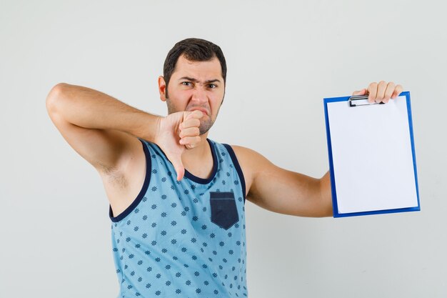 Young man holding clipboard, showing thumb down in blue singlet and looking discontent. 