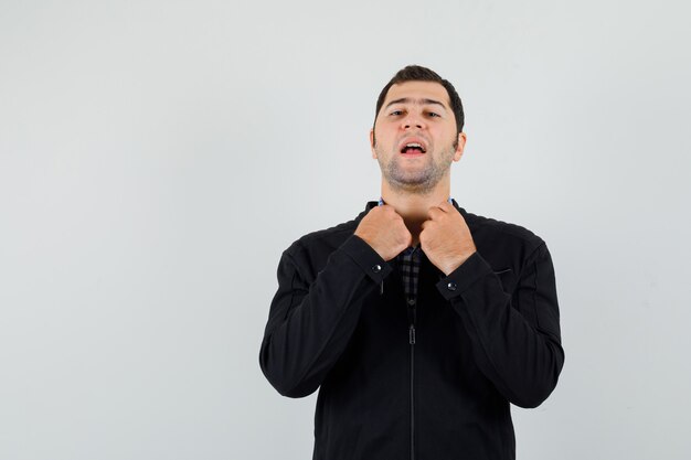 Young man holding collar of his shirt in shirt, jacket and looking proud. 