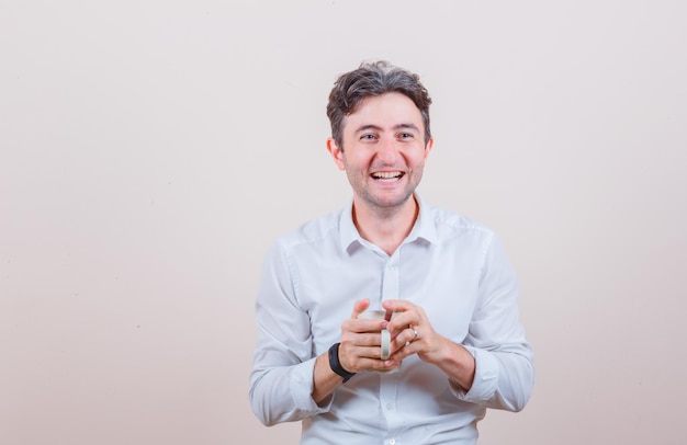 Young man holding cup of drink in white shirt and looking blissful