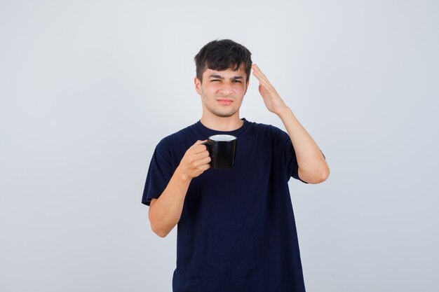 お茶を持って、黒いTシャツで手を上げて、困惑しているように見える若い男、正面図。