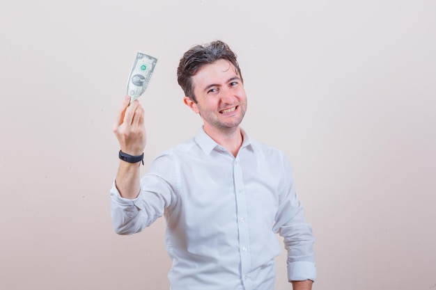 Young man holding dollar bill in white shirt and looking cheerful