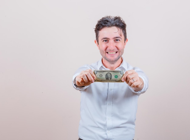 Free photo young man holding dollar bill in white shirt and looking happy