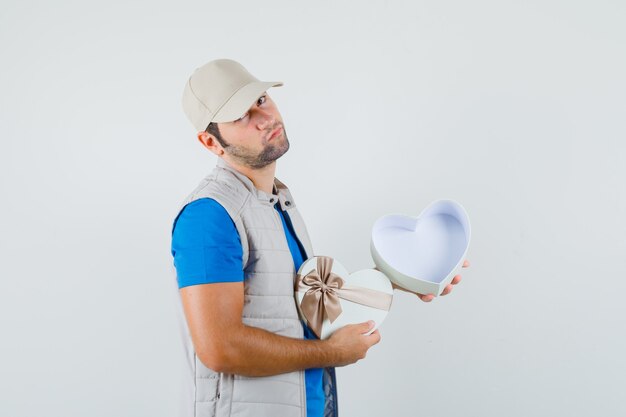 Young man holding empty gift box in t-shirt, jacket and looking pensive. front view.