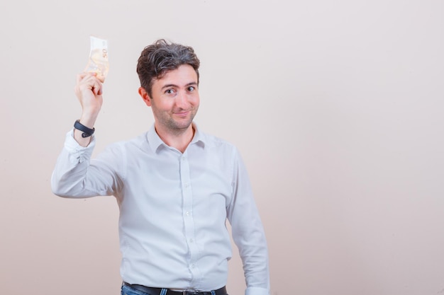 Young man holding euro banknote in white shirt, jeans and looking glad