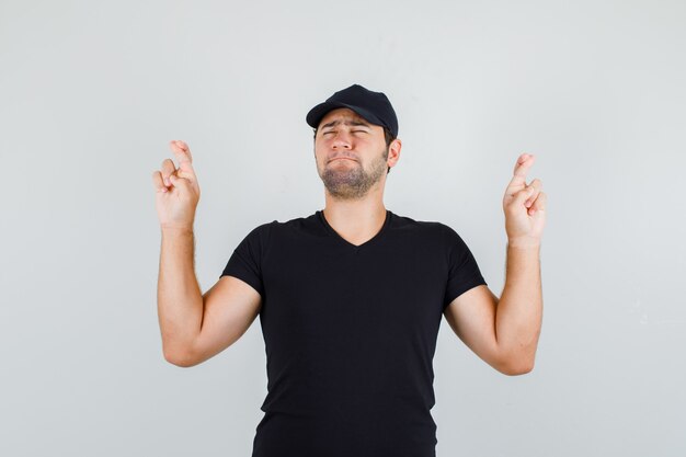 Young man holding fingers crossed in black t-shirt