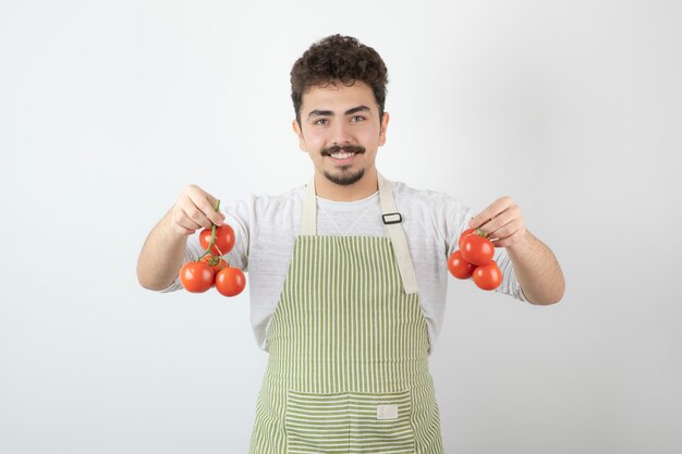 Молодой человек держит свежие помидоры рукой и улыбается в камеру.