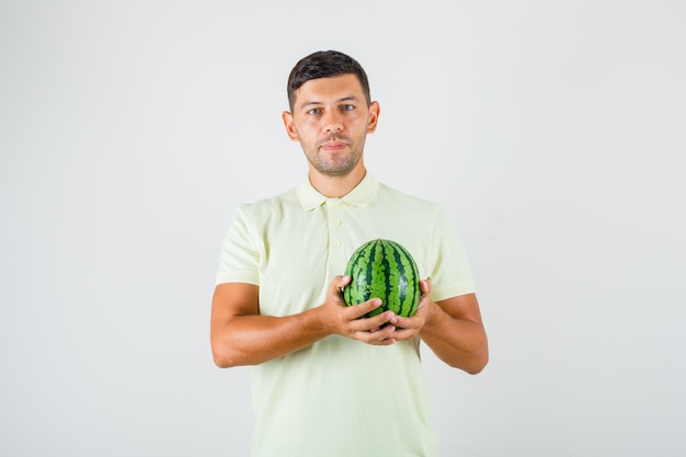 Young man holding fresh watermelon in t-shirt and looking glad.