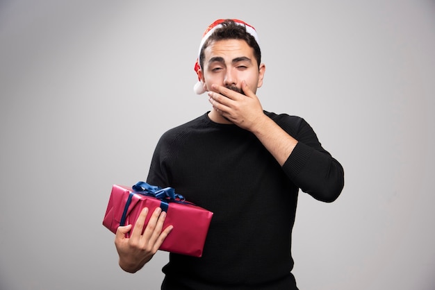 Foto gratuita un giovane uomo in possesso di una confezione regalo su un muro grigio.