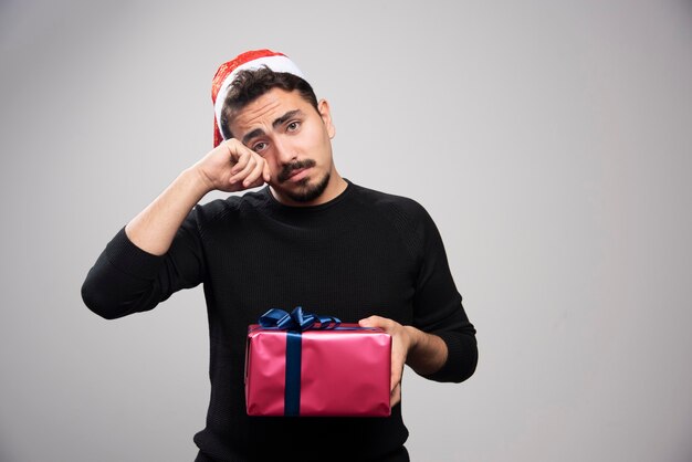 A young man holding a gift box over a gray wall.