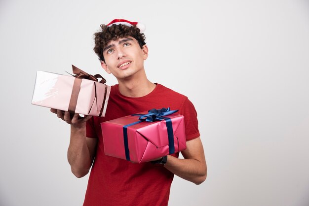 Молодой человек держит подарочные коробки и смотрит вверх.