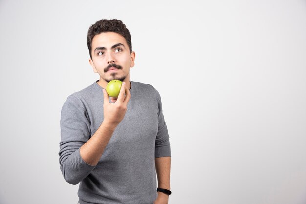 Young man holding green apple and thinking.