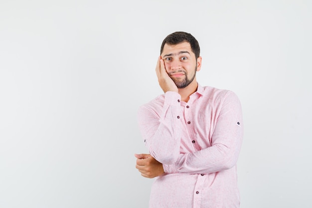 Young man holding hand on cheek in pink shirt and looking pensive