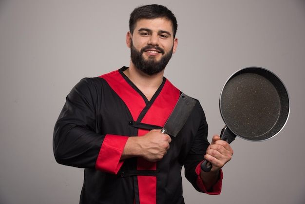 Young man holding in hand dark pan .