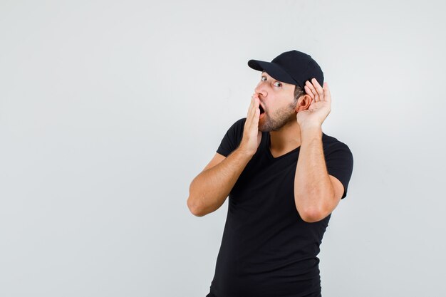 Young man holding hand behind ear in black t-shirt