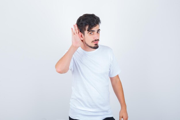 Молодой человек держит руку за ухом в футболке и выглядит уверенно