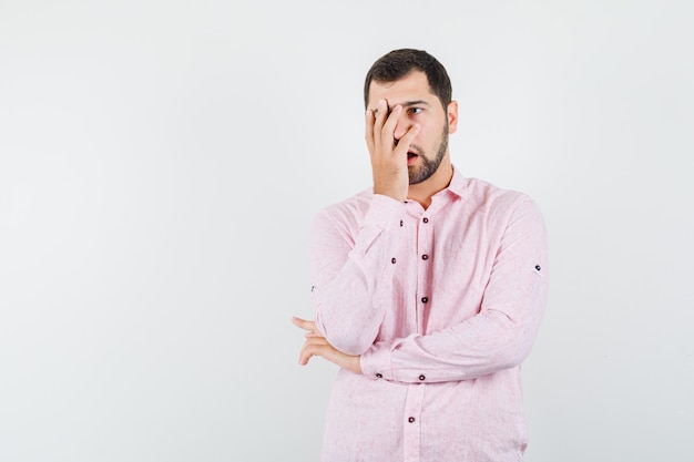 Young man holding hand on face in pink shirt and looking sorry