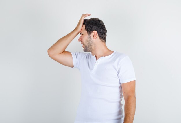 Young man holding hand on forehead in white t-shirt and looking regretful