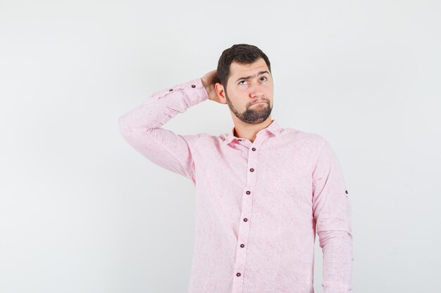 Young man holding hand behind head in pink shirt and looking pensive