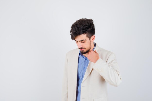 Young man holding hand on jacket in blue t-shirt and white suit jacket and looking serious