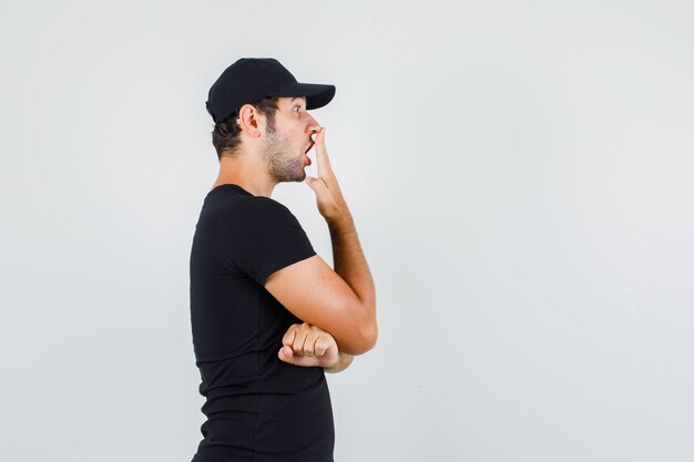 Young man holding hand on mouth in black t-shirt