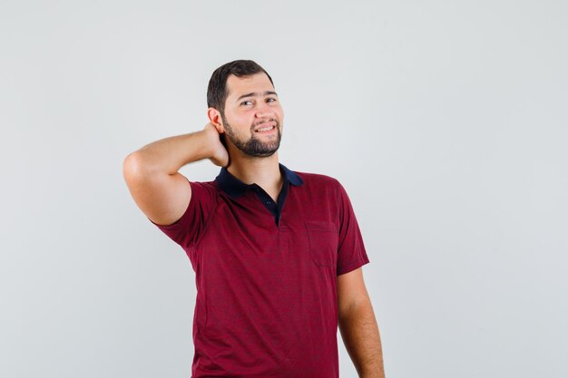 Young man holding hand on neck in t-shirt and looking elegant , front view.