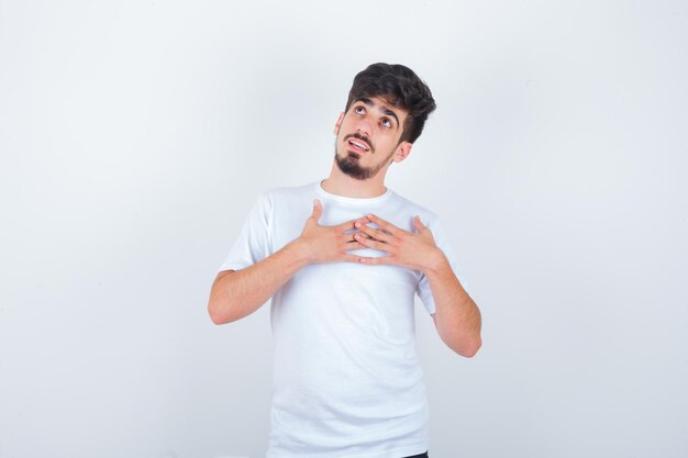 Young man holding hands on chest in t-shirt and looking hopeful