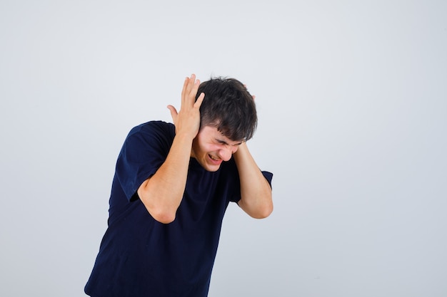 Free photo young man holding hands on ears in black t-shirt and looking irritated. front view.