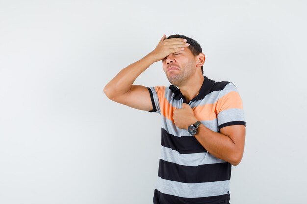 Young man holding hands on forehead and chest in t-shirt and looking unwell