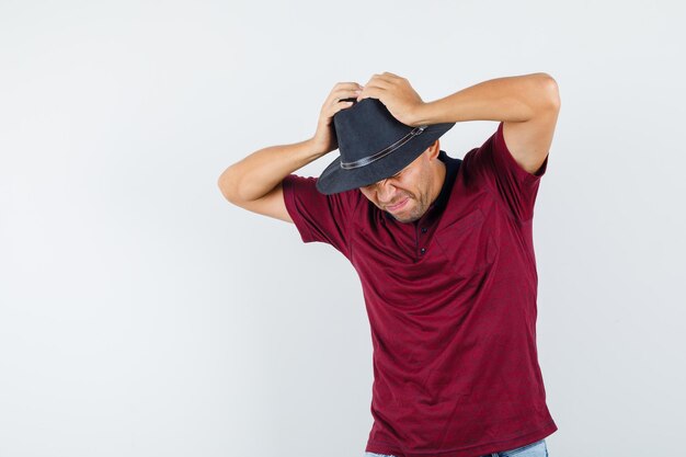 Young man holding hands on head in t-shirt, hat and looking regretful. front view.