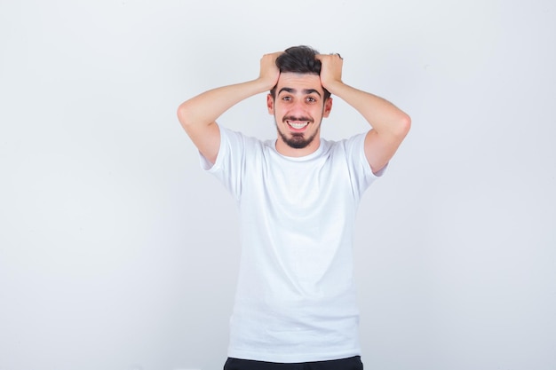 Young man holding hands on head while posing in t-shirt and looking joyful