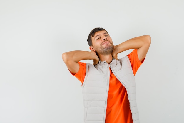 Free photo young man holding hands on neck in t-shirt, jacket and looking relaxed. front view.