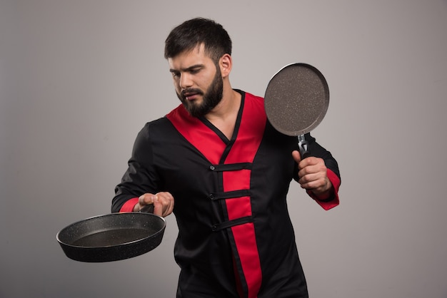 Young man holding in hands two dark pans .