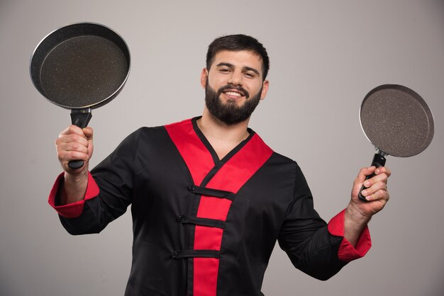 Young man holding in hands two dark pans .