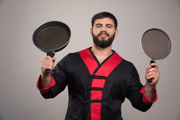 Young man holding in hands two dark pans .