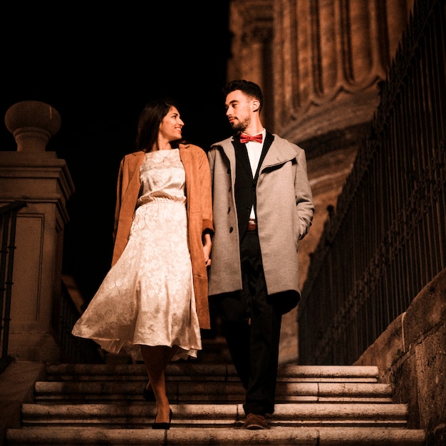 Young man holding hands with elegant woman and going down on steps