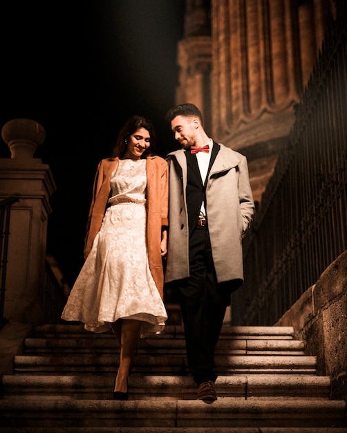 Free photo young man holding hands with happy elegant woman and going down on steps
