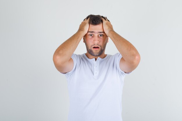 Young man holding head with hands in white t-shirt and looking stressful