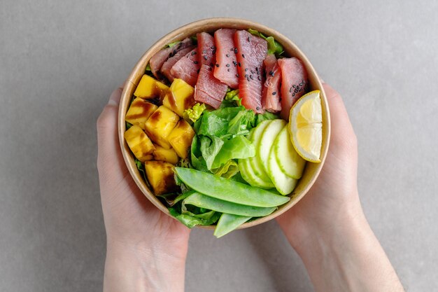 Young man holding Healthy raw Tuna bowl with vegetables served in paper bowl