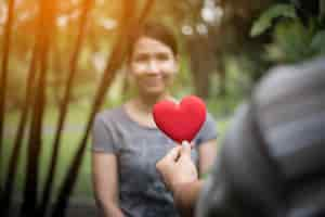 Free photo young man holding heart shaped valentine card and looking while standing  with girlfriend.