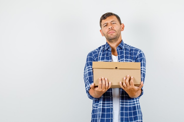 Free photo young man holding heavy cardboard box in shirt , front view.