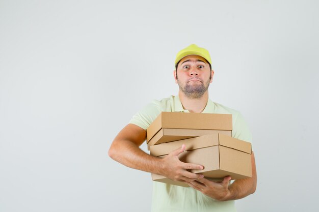 Young man holding heavy cardboard boxes in t-shirt cap  