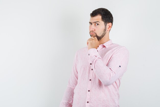 Young man holding his chin in pink shirt and looking pensive 