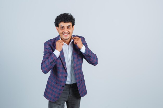 Young man holding his collar in shirt, jacket, pants and looking handsome. front view.