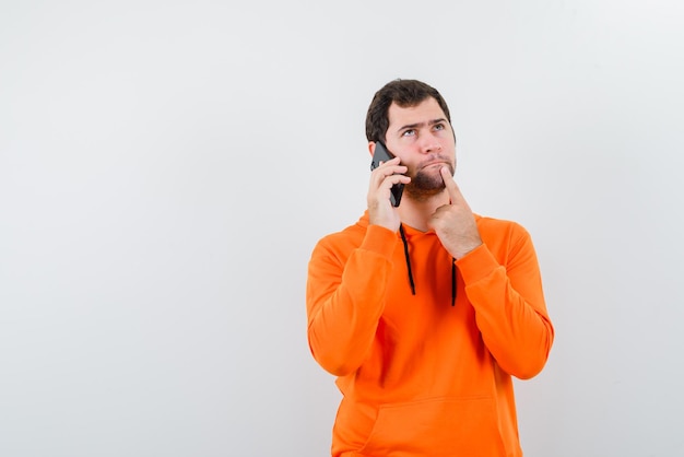 Молодой человек держит палец у рта и звонит кому-то по телефону на белом фоне