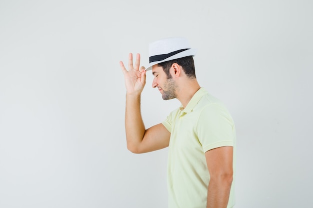 Young man holding his hat in t-shirt and looking elegant 