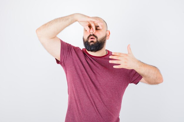 Young man holding his left hand on elbow, thinking about something in pink t-shirt and looking irritated , front view.